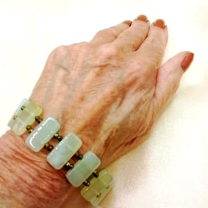 May include: A bracelet featuring rectangular, pale green, translucent stone beads arranged in a row, connected by small, dark metallic spacer beads. The design consists of five smooth, polished rectangular segments linked together in a linear pattern.