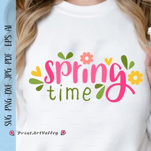 Könnte beinhalten: Ein weißes T-Shirt mit dem Text "spring time" in rosa Schrift mit grünen Blättern und gelben und rosa Blumen.
