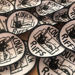 May include: A collection of white and black patches. Each patch features a black illustration of a guitar leaning against a couch, with the words "COUCH RIFFS" in a bold, stylized font. The patches have a black border.
