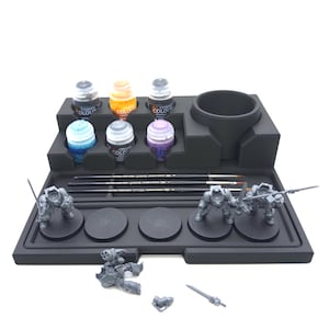 May include: A black paint station with six paint bottles, paint brushes, and miniature figurines. The paint bottles are filled with various colors, including blue, orange, and purple. The figurines are gray and appear to be part of a tabletop game.
