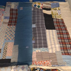May include: A rectangular patchwork quilt constructed from various fabric scraps, including blue denim, plaid, gingham, and floral patterns. The quilt features a mix of solid colors and diverse prints stitched together in a multi-panel design.