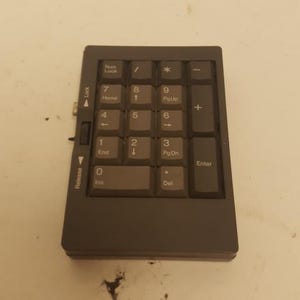 May include: A dark gray numeric keypad with white lettering. The keypad includes number keys, function keys, and an Enter key. A switch on the side is labeled "Lock" and "Release".