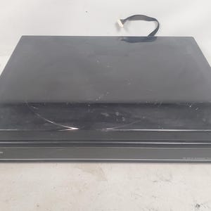 Może przedstawiać: Czarny system gramofonowy Panasonic 33-Series Automatic. Górna część jest błyszcząca czarna z kilkoma zadrapaniami. Na przednim panelu znajduje się logo Panasonic i informacje o modelu w kolorze białym.