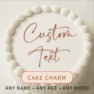 May include: A round white cake with a piped white frosting border. The words "Custom Text" are written in a brown script font on the cake. A red and white banner at the bottom reads "CAKE CHARM". The text "ANY NAME • ANY AGE • ANY WORD" is below the banner.