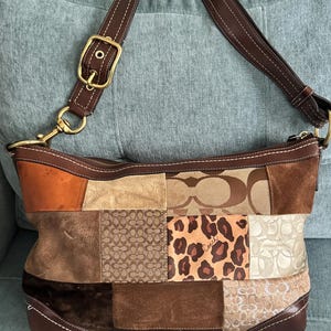 May include: A Coach shoulder bag featuring a patchwork design of brown, tan, and cream leather, suede, and canvas panels. The bag includes a leopard print section, a brown leather adjustable strap with brass hardware, and a top zipper closure.