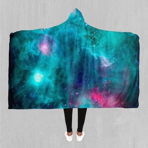 Puede incluir: Una manta con capucha con estampado de galaxia que presenta nebulosas azules, rosas y moradas y estrellas.