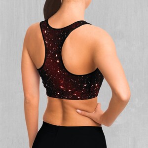 Op de afbeelding: Een zwarte sportbeha met een galaxy print met rode, witte en blauwe sterren. De beha heeft een racerback-stijl.