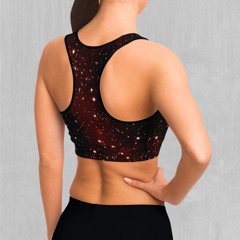 Op de afbeelding: Een zwarte sportbeha met een galaxy print met rode, witte en blauwe sterren. De beha heeft een racerback-stijl.