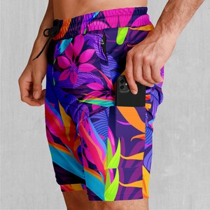 Puede incluir: Pantalones cortos vibrantes y coloridos con un estampado floral tropical en tonos morado, rosa, azul, naranja y verde. Los pantalones cortos tienen una cintura con cordón y un bolsillo con un teléfono inteligente negro.