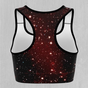 Op de afbeelding: Een zwarte sportbeha met een galaxy print met rode, witte en blauwe sterren op een donkere achtergrond.