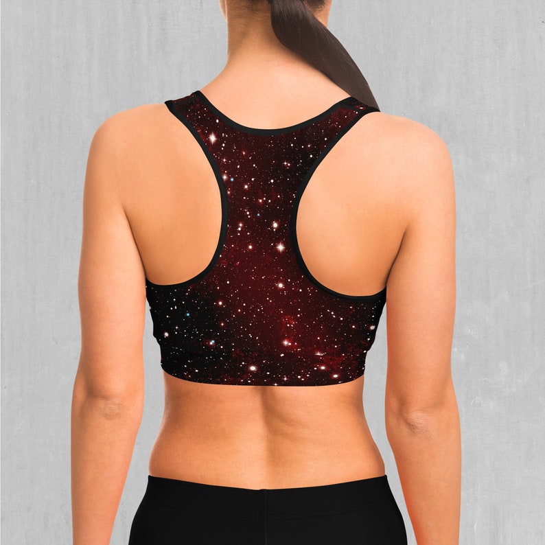 Op de afbeelding: Een zwarte sportbeha met een galaxy print in rood, wit en zwart. De beha heeft een racerback-stijl.