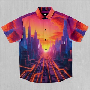 Puede incluir: Una camisa de manga corta con botones con un estampado de ciudad colorido. El estampado presenta una ciudad futurista con edificios altos y una puesta de sol brillante en el fondo.