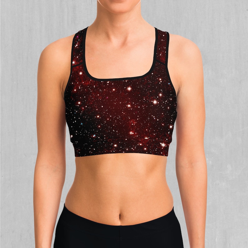 Op de afbeelding: Een zwarte sportbeha met een rode en zwarte galaxy print. De beha heeft een racerback-stijl en is gemaakt van een rekbaar, comfortabel materiaal.