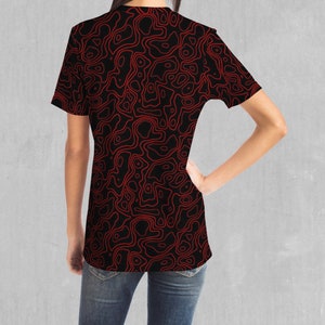 May include: A black t-shirt with a red abstract pattern. The pattern is made up of thin lines that create a swirling, organic design.
