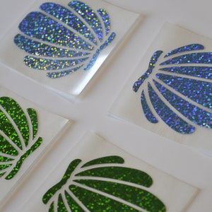 Op de afbeelding: Vier iriserende schelp stickers, twee groen en twee blauw, op wit papier.