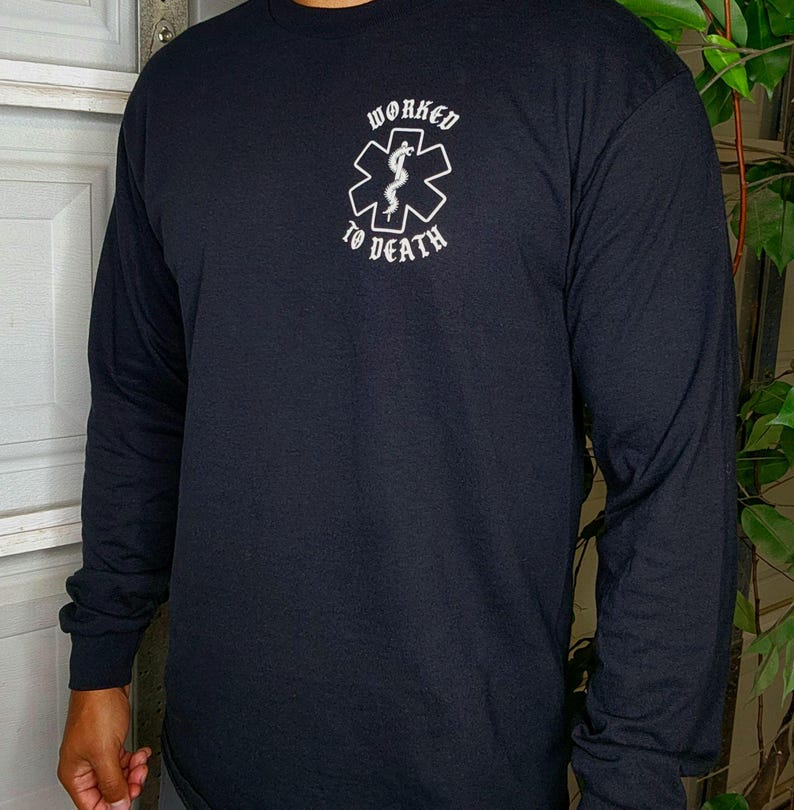 May include: Black long-sleeve shirt with the text "WORKED TO DEATH" above a white medical symbol. The shirt is made of a soft material and has long sleeves. The design is centered on the chest.