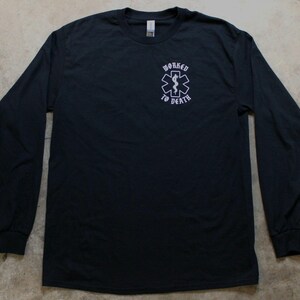 May include: Black long-sleeve shirt with a crew neck. The shirt features a white graphic of a medical symbol with a snake and staff, and the words "WORKED TO DEATH" in a stylized font.