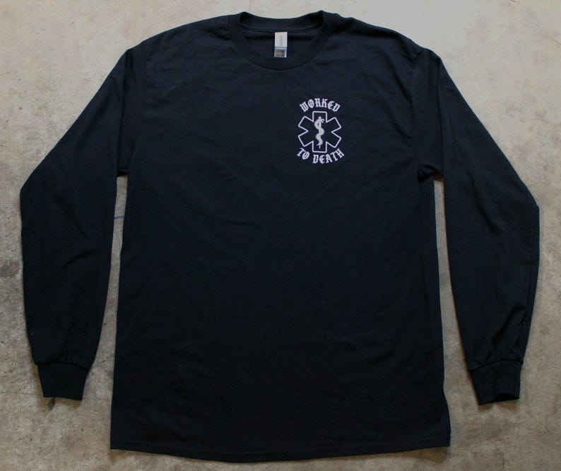 May include: Black long-sleeve shirt with a crew neck. The shirt features a white graphic of a medical symbol with a snake and staff, and the words "WORKED TO DEATH" in a stylized font.
