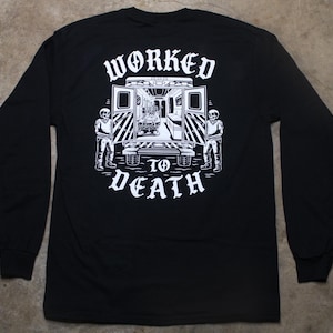 May include: Black long-sleeve shirt with a white graphic on the back. The graphic features an ambulance with skeletons and the words "WORKED TO DEATH" in a gothic font. The shirt has a crew neck and long sleeves.