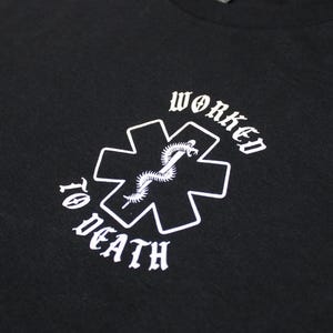 May include: Black t-shirt with a white graphic. The graphic features a medical cross with a snake and the words "WORKED TO DEATH" in a gothic font. The shirt is made of a soft material.