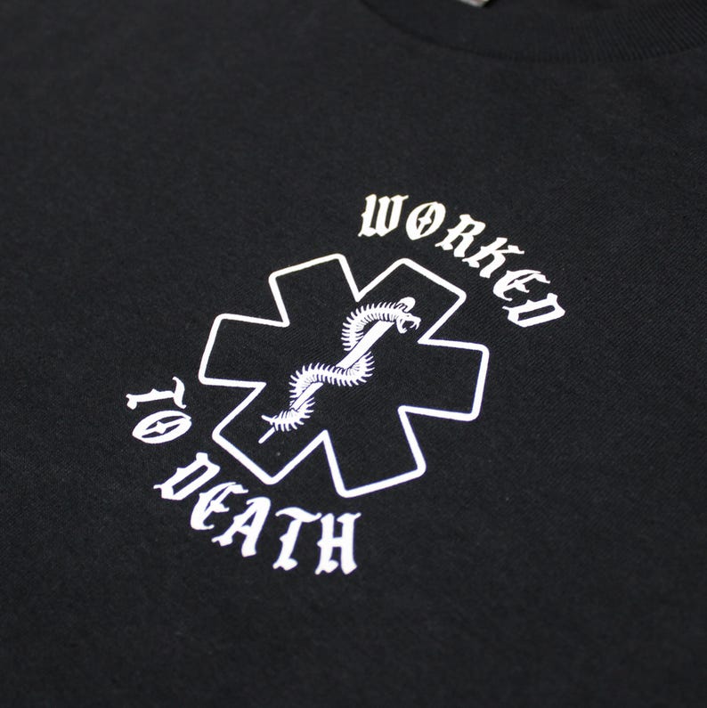 May include: Black t-shirt with a white graphic. The graphic features a medical cross with a snake and the words "WORKED TO DEATH" in a gothic font. The shirt is made of a soft material.