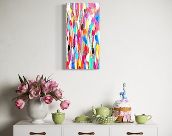 Op de afbeelding: Een kleurrijk abstract schilderij met verticale penseelstreken in rood, blauw, geel en roze hangt boven een witte console. De tafel is versierd met een vaas met roze tulpen en een decoratieve taart.