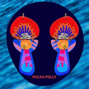 以下が含まれることがあります： 幾何学模様のカラフルなステートメントイヤリングのペア。イヤリングは、赤、オレンジ、ピンク、ブルー、ゴールドの色の重ねられた形で作られています。イヤリングはグリッターで飾られており、ユニークで抽象的なデザインになっています。