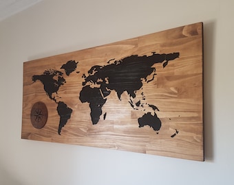 May include: A wooden wall art piece featuring a black silhouette of the world map with a compass design in the lower left corner.
