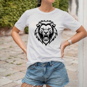 May include: White t-shirt featuring a black lion head graphic. The lion graphic is detailed with a fierce expression and open mouth. The shirt is a classic crew neck style and is paired with denim shorts.