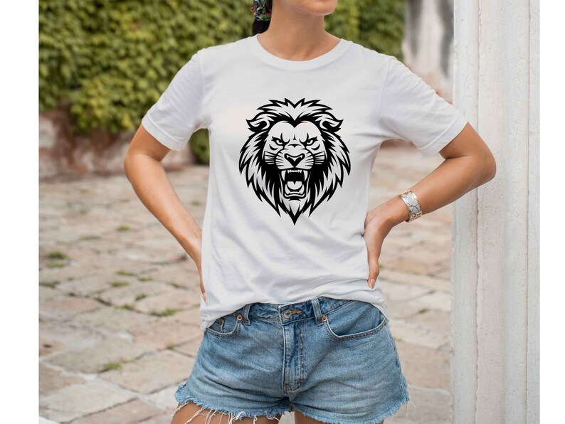 May include: White t-shirt featuring a black lion head graphic. The lion graphic is detailed with a fierce expression and open mouth. The shirt is a classic crew neck style and is paired with denim shorts.