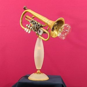 Op de afbeelding: Een gouden trompetlamp met een witte, matglazen voet en een heldere glazen gloeilamp. De trompet is omhoog gericht en de gloeilamp bevindt zich aan het einde van de schelp.