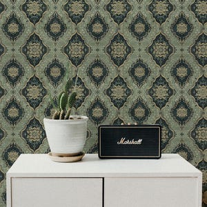 May include: A white cabinet with two doors against a backdrop of green and gold patterned wallpaper. A small potted cactus and a black Marshall speaker are on top of the cabinet.