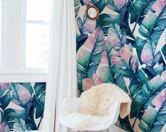 May include: A white rocking chair with a fluffy white sheepskin throw on the seat. The chair is in a room with a white wall covered in a tropical leaf wallpaper with pink and green hues.