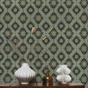 May include: A green and gold patterned wallpaper with a repeating geometric design. Two white ceramic vases and a gold metal watering can are arranged on a wooden table in front of the wallpaper.