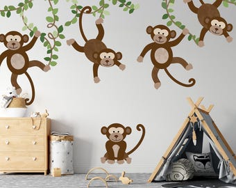 May include: A whimsical wall decal set featuring brown cartoon monkeys hanging from green vines. The set includes several monkeys in various poses, creating a playful jungle theme. A teepee and wooden furniture are also in the scene.