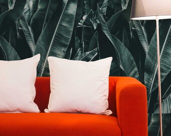 May include: A red sofa with two white pillows against a dark green tropical leaf patterned wall. A silver floor lamp with a black lampshade is in the corner.