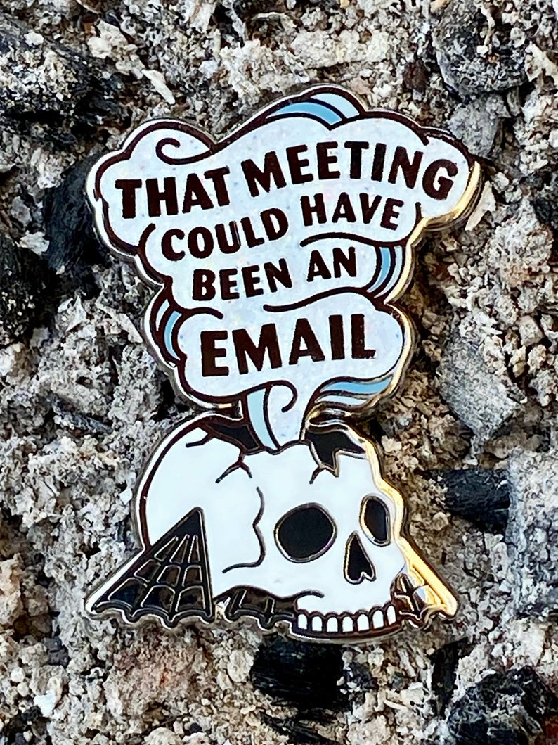 May include: A white enamel pin with a skull and a speech bubble that says "That meeting could have been an email".