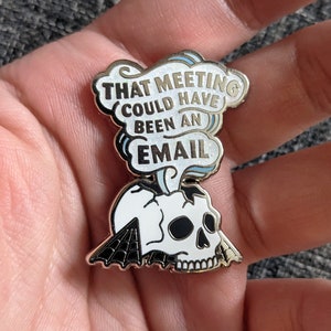 May include: A gold-toned enamel pin with a white skull and a speech bubble that reads "That meeting could have been an email".