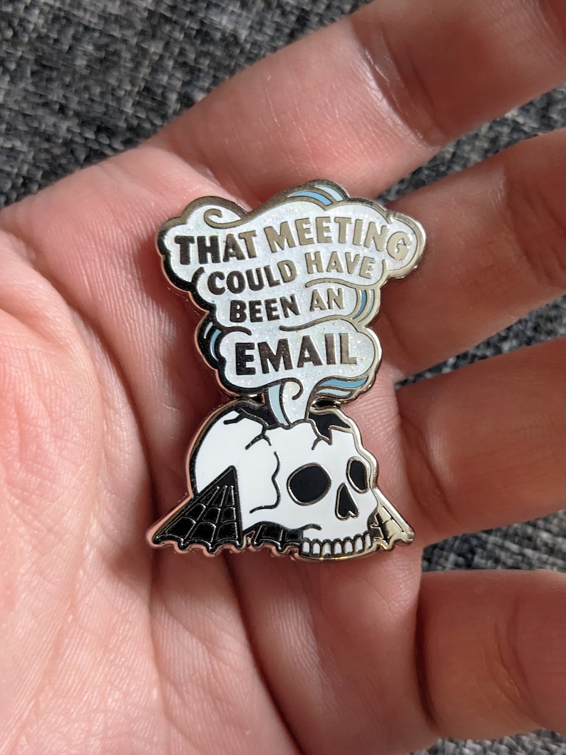 May include: A gold-toned enamel pin with a white skull and a speech bubble that reads "That meeting could have been an email".