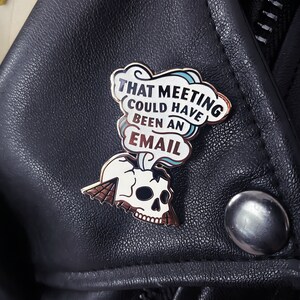 May include: A gold and white enamel pin with a skull and a speech bubble that says "That meeting could have been an email".