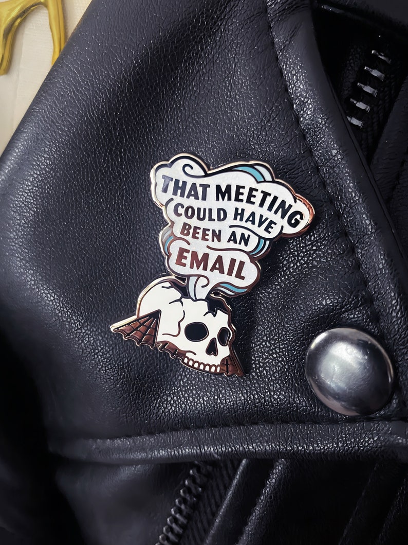 May include: A gold and white enamel pin with a skull and a speech bubble that says "That meeting could have been an email".