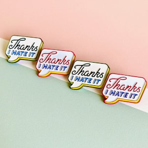 May include: Four enamel pins with a speech bubble design. Each pin says "Thanks I Hate It" in a retro font. The pins are in different colors: blue, green, yellow, and red.