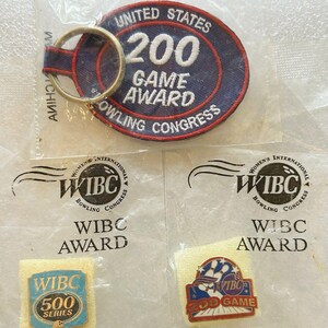 May include: A collection of bowling awards and pins. Includes a blue and red patch keychain with "UNITED STATES 200 GAME AWARD BOWLING CONGRESS" text, and two WIBC award pins. One pin reads "WIBC 500 SERIES".