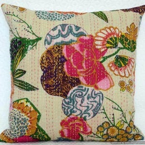 May include: Cream-colored square pillow with a vibrant floral design. The pillow features large pink flowers, green leaves, and circular patterns in teal, brown, and gold. The design is stitched onto the fabric.
