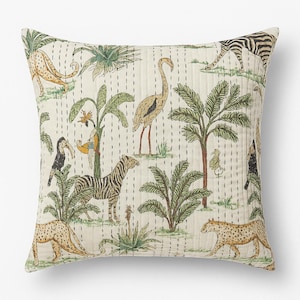 以下が含まれることがあります： クリーム色の背景にジャングルシーンが描かれた正方形のクッション。デザインには、シマウマ、ヒョウ、鳥、ヤシの木が緑、茶色、タンの色合いで描かれています。クッションは、垂直のステッチが施されたキルトの質感です。