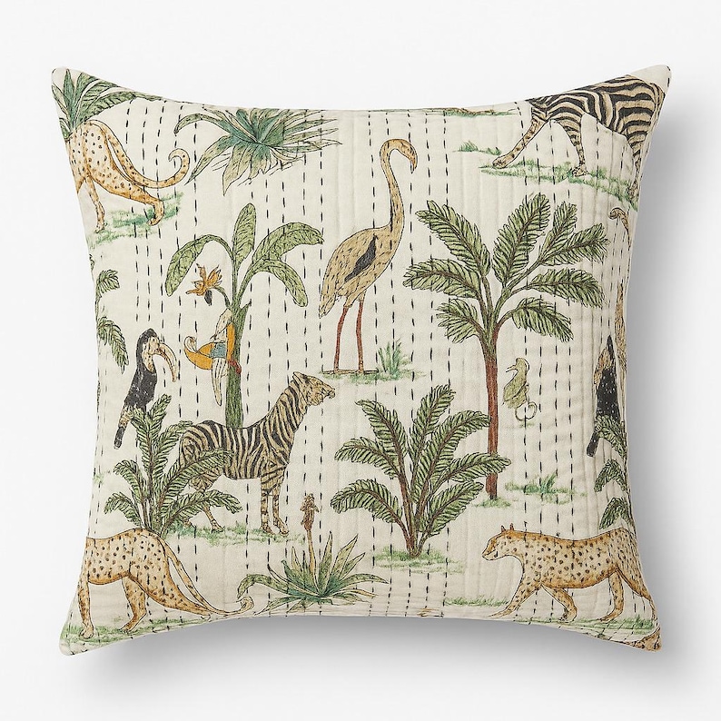 May include: Square throw pillow with a cream background featuring a jungle scene. The design includes zebras, leopards, birds, and palm trees in shades of green, brown, and tan. The pillow has a quilted texture with vertical stitching.