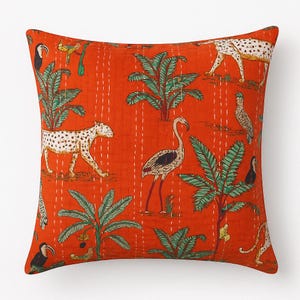 Puede incluir: Cojín cuadrado naranja con un patrón repetido de leopardos, flamencos, tucanes y palmeras. El diseño está cosido con hilo blanco. El cojín tiene un tema tropical.