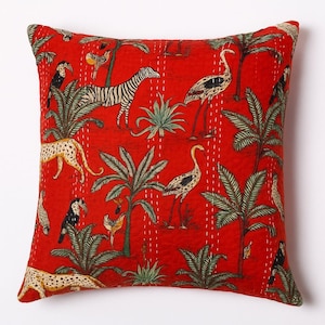 May include: Red square throw pillow with a vibrant jungle scene. The pillow features a zebra, leopard, birds, and palm trees. The design is printed on the fabric and stitched with white thread. The pillow has a solid red background.