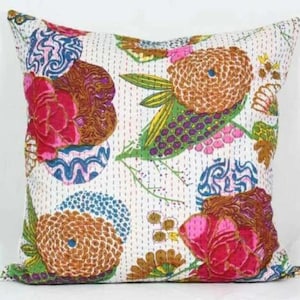May include: Square decorative pillow with a white background and a colorful floral pattern. The design features large flowers in shades of pink, brown, and orange, with green leaves and blue accents. The pillow has a stitched texture.