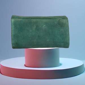 May include: A dark green suede clutch purse on a white and pink platform.